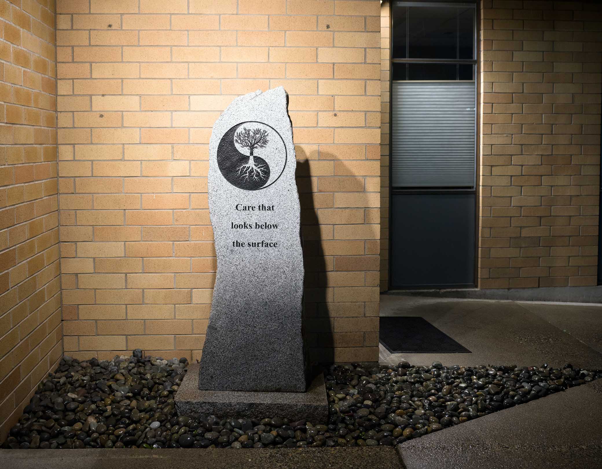Granite stone monument at clinic entrance - yin-yang tree with roots and the inscription: Care that looks below the surface